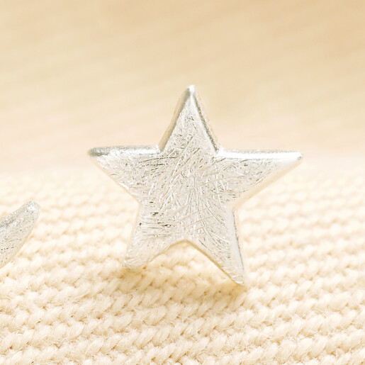 Close-up of a brushed silver star stud earring on cream woven fabric