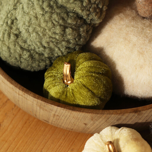 Mini green velvet pumpkin nestled in a wooden bowl with textured decorative pumpkins.