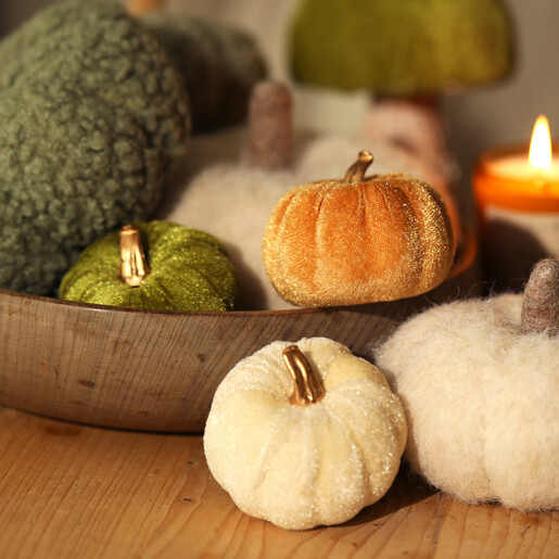 Assorted colourful velvet and plush pumpkin decorations displayed with a wooden bowl and candle.