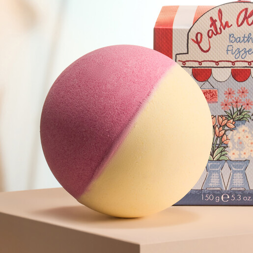Close-up of the two-tone pink and yellow round bath fizzer next to packaging