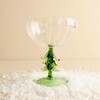 Clear fluted glass cocktail coupe with sculpted green Christmas tree stem set in faux snow