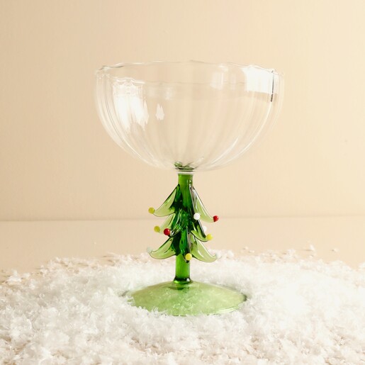 Clear fluted glass cocktail coupe with sculpted green Christmas tree stem set in faux snow