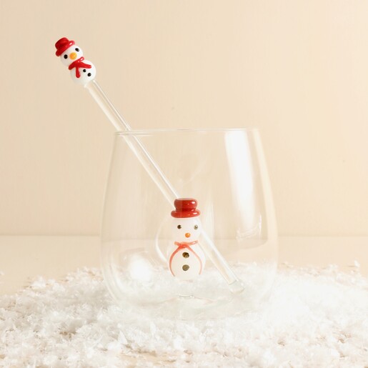 Glass snowman cocktail stirrer inside a matching snowman tumbler on faux snow