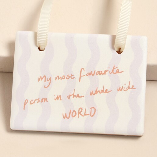 Close-up of ceramic hanging plaque with lilac wavy stripes and peach text.