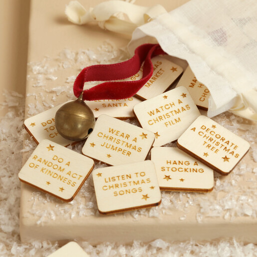 Engraved wooden Christmas countdown activity tokens spilling out of a fabric pouch with a bell