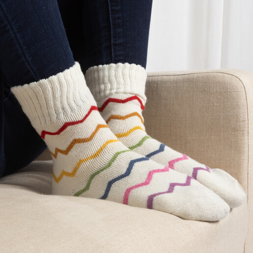 Person wearing cream knit socks with colourful zig-zag stripes resting on a chair