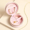Open pink jewellery case showing interior ring rolls and compartments holding gold jewellery