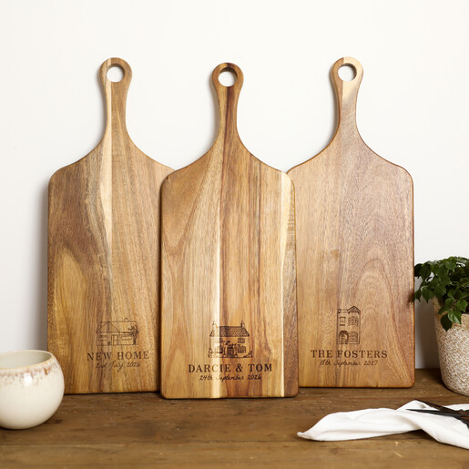 Three personalised acacia wood paddle boards standing upright with different house illustrations