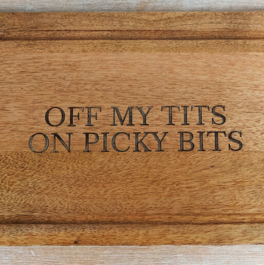 Close-up of engraved text reading off my tits on picky bits on wooden board