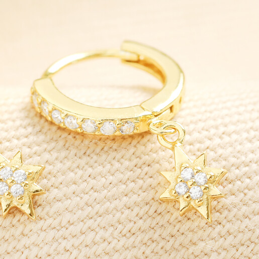 Close-up of gold-plated crystal star charm huggie hoop earring on woven fabric