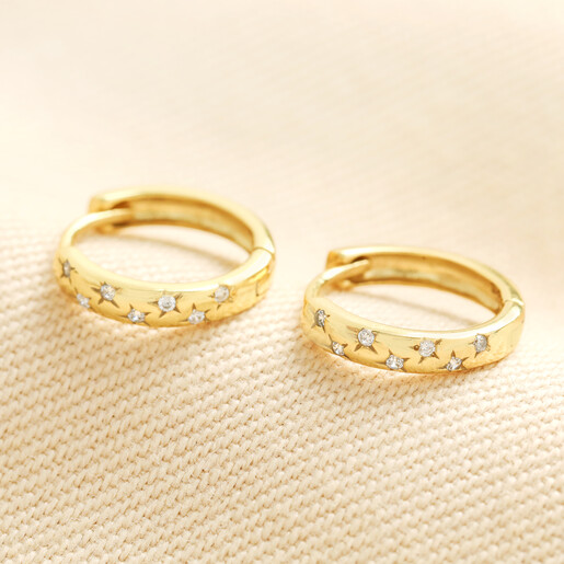 Pair of gold sterling silver scattered star huggie hoop earrings on cream fabric