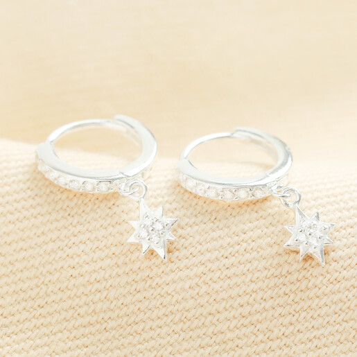 Pair of sterling silver huggie hoop earrings featuring sparkling crystal star charms.