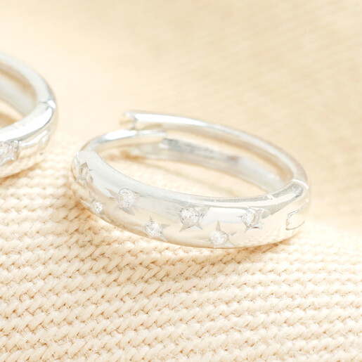 Close-up of sterling silver huggie hoop earring with star and crystal details