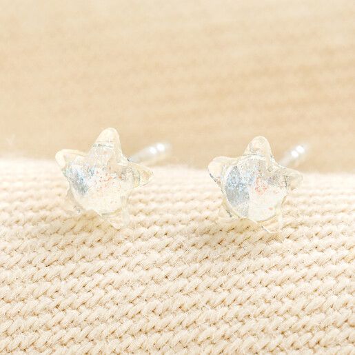 Pair of sterling silver rainbow star stud earrings displayed on textured beige fabric.