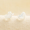 Delicate clear crystal heart stud earrings displayed on woven neutral fabric