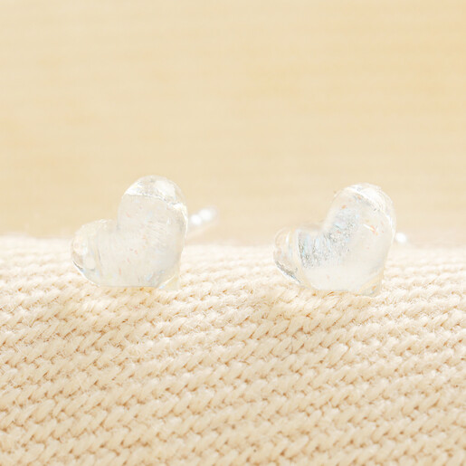 Delicate clear crystal heart stud earrings displayed on woven neutral fabric