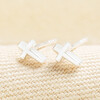 A pair of polished sterling silver cross stud earrings resting on cream fabric.
