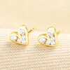 Pair of gold sterling silver crystal heart stud earrings on textured fabric