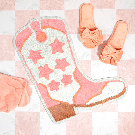 Pink and cream cowboy boot tufted bath mat styled on tiled bathroom floor with slippers
