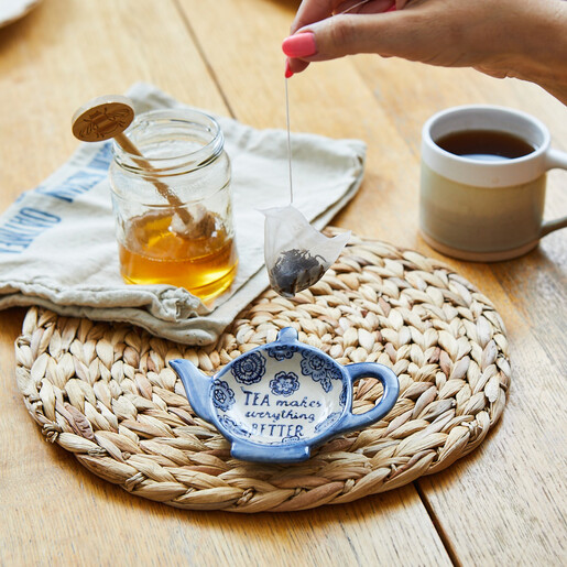 Teabag held above the blue and white teapot tea tidy on a table