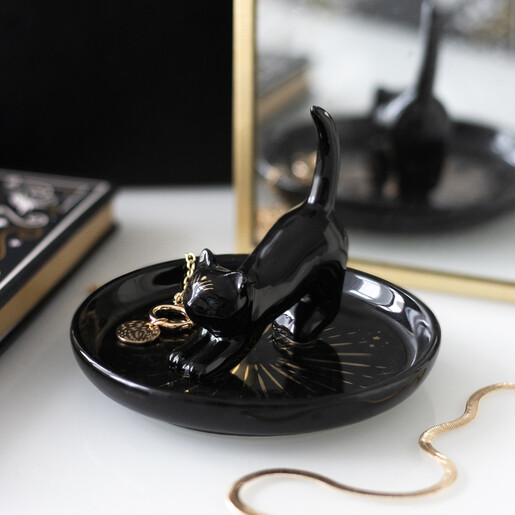 Black ceramic cat trinket dish holding jewellery on a table near a mirror