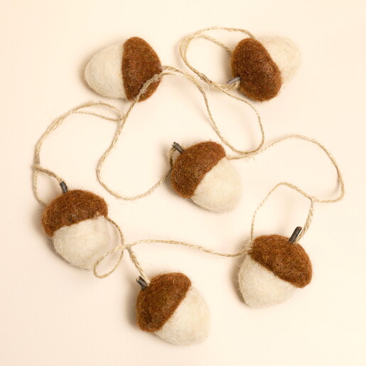 Neutral felt mini acorn garland arranged neatly against a warm cream background
