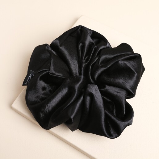 Oversized black satin hair scrunchie laid flat on a square stone plinth.