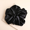 Oversized black satin hair scrunchie laid flat on a square stone plinth.