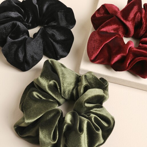 Close-up of three festive velvet hair scrunchies in black, green, and red