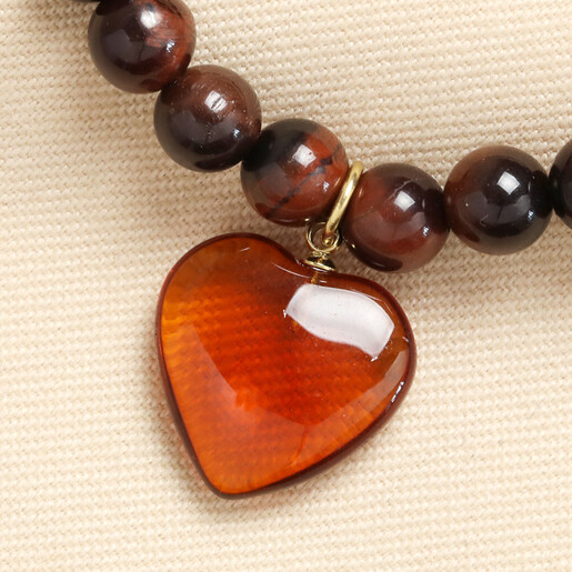 Close up of glossy amber glass heart charm on brown stone beaded bracelet