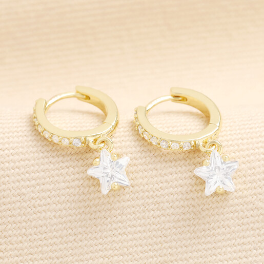 Pair of gold crystal star huggie hoop earrings on fabric background