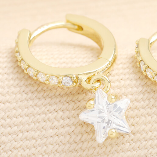 Close-up of gold crystal star charm dangling from huggie hoop earring