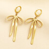 Gold stainless steel huggie hoop earrings with large hanging ribbon bow charms