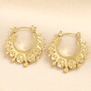 Pair of gold stainless steel boho creole hoop earrings on textured beige background