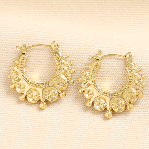 Pair of gold stainless steel boho creole hoop earrings on textured beige background