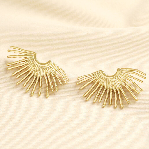 A pair of gold oversized fan stud earrings with textured sunburst rays on fabric