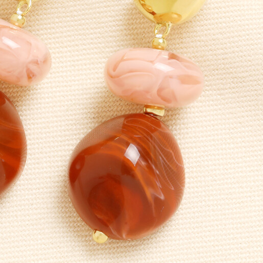 Close-up of marbled pink and terracotta red drop charms on gold earring