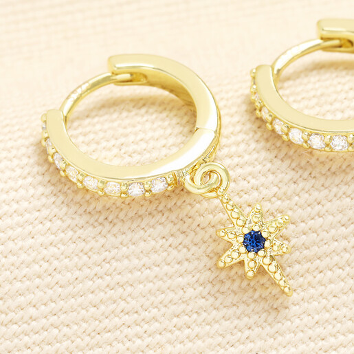 Close-up of gold huggie hoop earring with dangling blue crystal star charm