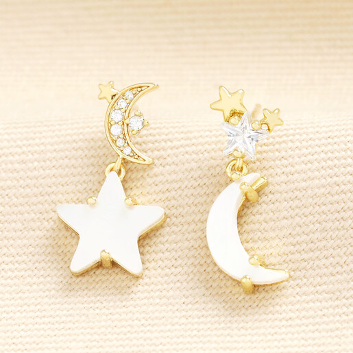 Mismatched gold celestial drop earrings with white shell star and moon charms.