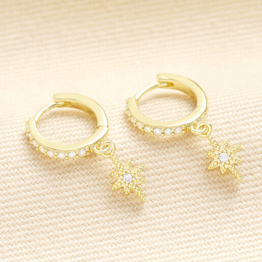 Pair of gold crystal star huggie hoop earrings on textured cream fabric