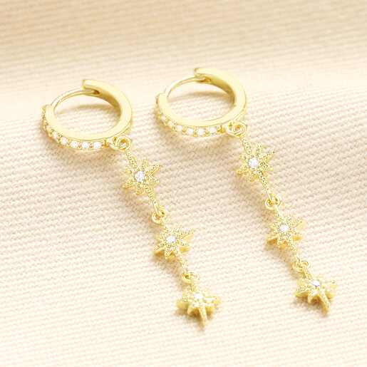 Pair of gold huggie hoop earrings with dangling crystal starburst charms on fabric