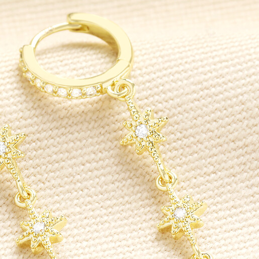 Close up of gold huggie hoop earring with sparkling crystal star drop charms