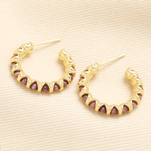 Pair of gold hoop earrings set with round purple stones on cream fabric
