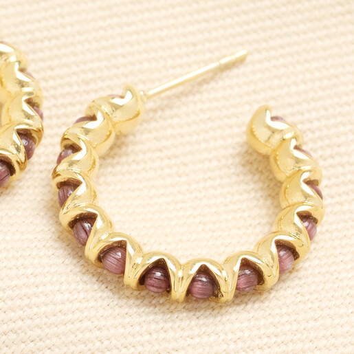 Close-up of wavy gold stainless steel hoop earring with purple stones
