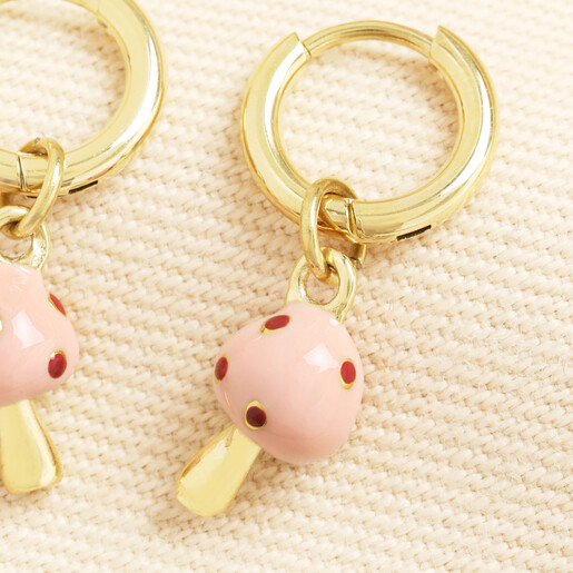Close up of a gold huggie hoop earring with a pink enamel mushroom charm