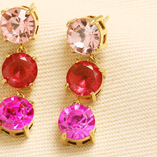 Close-up of gold drop earrings with pink and red round faceted crystals.
