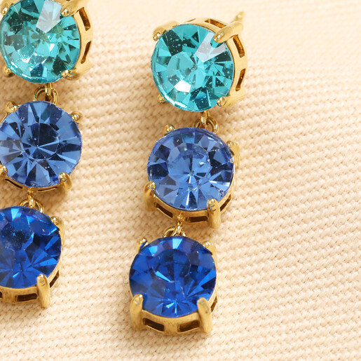 Close up of blue round triple gem drop earrings in gold settings