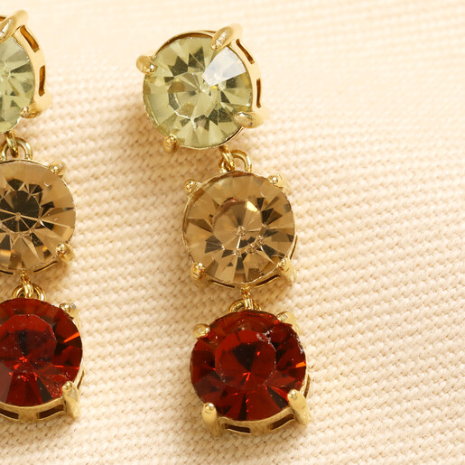 Close-up of brown and amber toned triple gem drop earrings on cream fabric