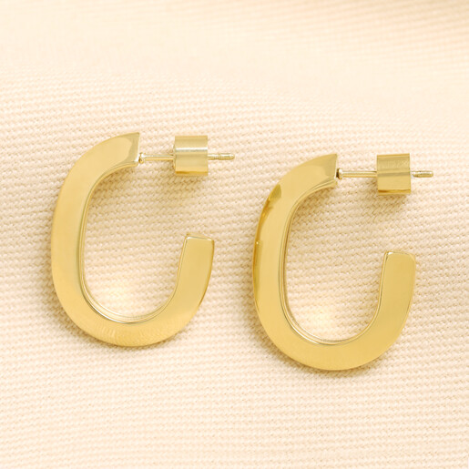 Pair of gold stainless steel chunky hoop earrings on neutral woven fabric