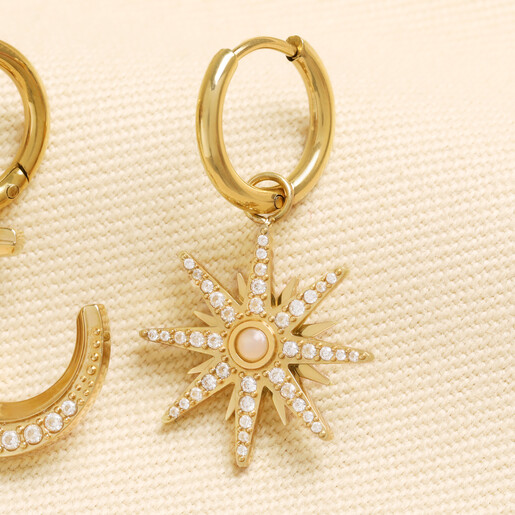 Close up of gold starburst charm huggie earring encrusted with clear cubic zirconia stones
